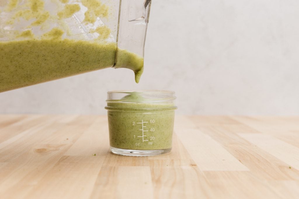 pouring broccoli puree into a glass jar 